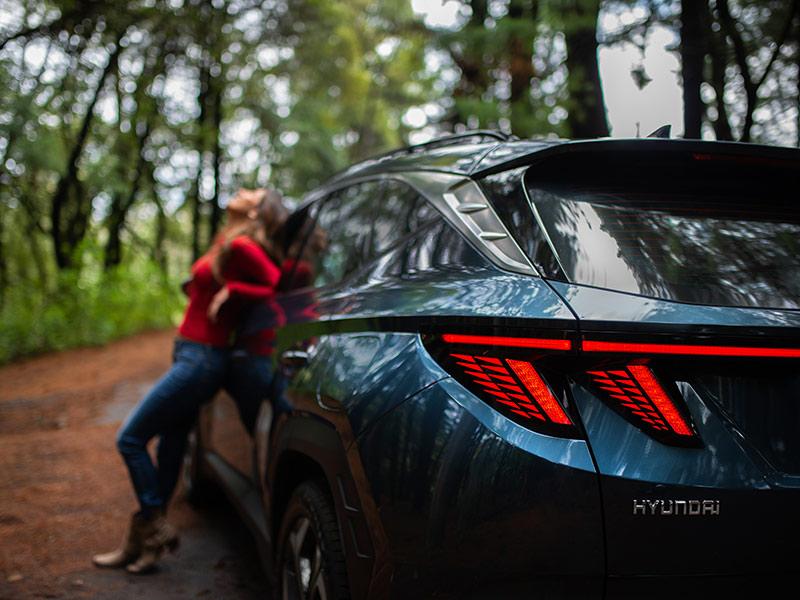 Mujer recargada en costado de Hyundai Tucson color azul en el bosque