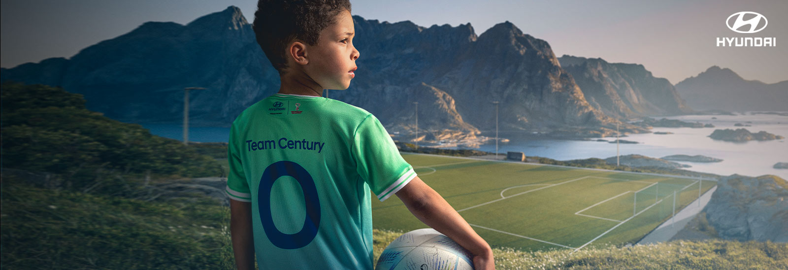 Niño con playera Goal of the Century y balón en la mano con una cancha de futbol al fondo