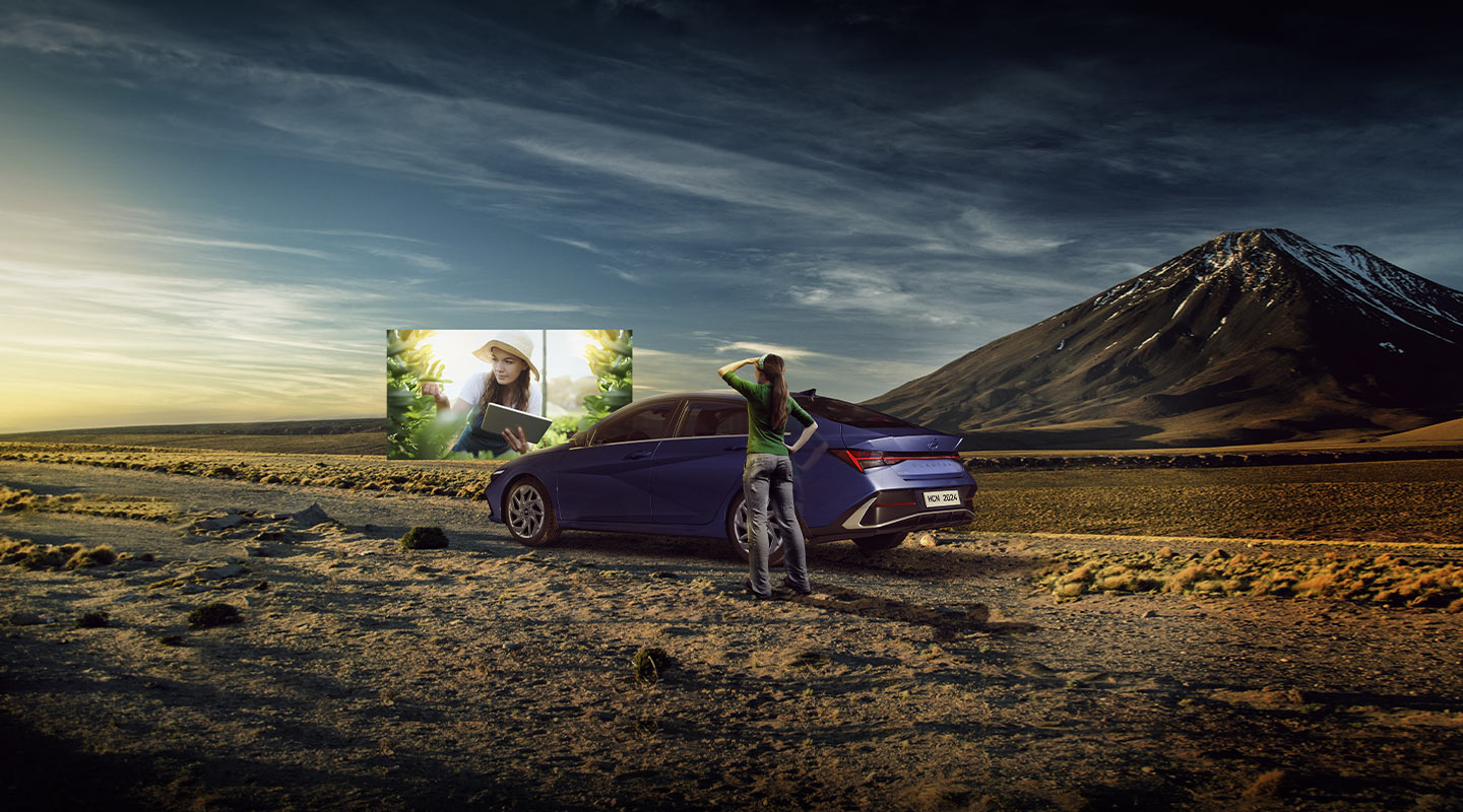 Mujer mirando al horizonte junto a Elantra híbrido azul en terreno desértico