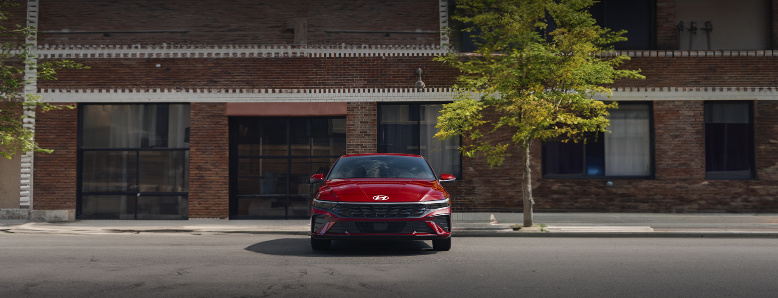 Vista frontal del nuevo Elantra 2024, en color rojo, estacionado en la calle