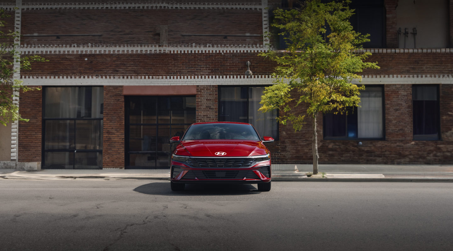 Vista frontal del nuevo Elantra 2024, en color rojo, estacionado en la calle