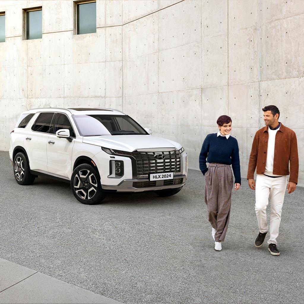 Hombre y mujer caminando juntos frente a una Hyundai Palisade color blanca