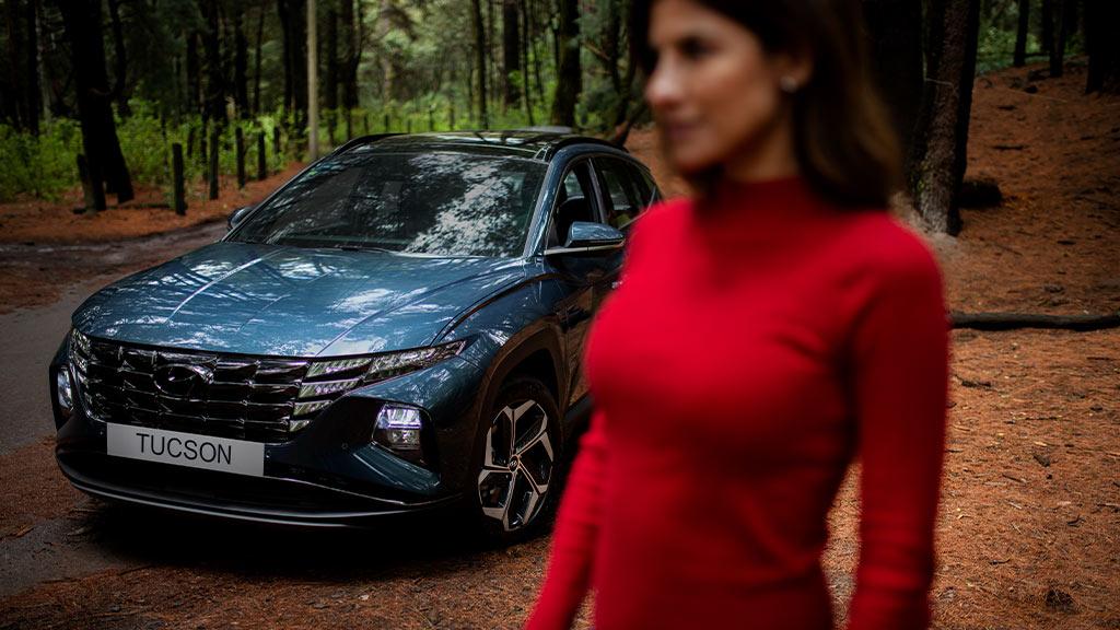 Mujer desenfocada en primer plano con Hyundai Tucson color azul en un bosque