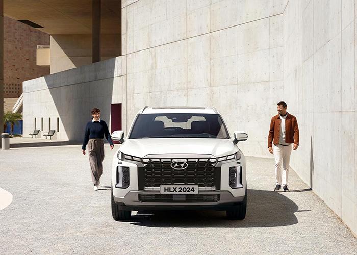 Hombre y mujer caminando por los costados de una Hyundai Palisade color blanca