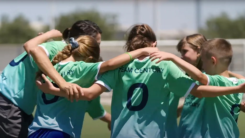 Niñas abrazandose con camisetas de goal century dentro de un partido