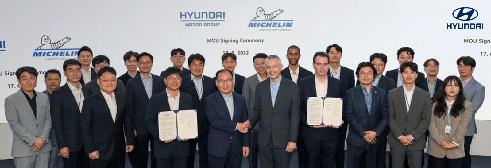 Ejecutivos de Hyundai y Michelin mostrando carpeta con acuerdo y en fila para fotografía