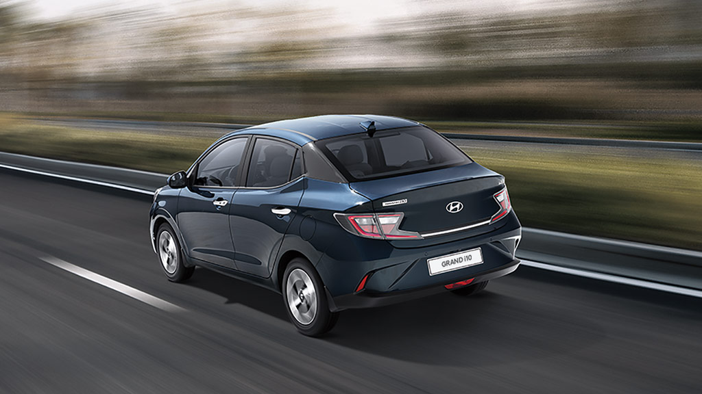 Vista tres cuartos trasera de Hyundai Grand i10 Sedán 2026 color azul circulando en la carretera